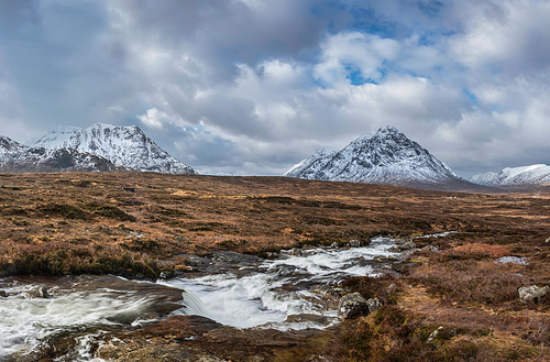 Beautiful Winter landscape image of River Etive in foreground with iconic snowcapped Stob Dearg Buachaille Etive Mor mountain in the background