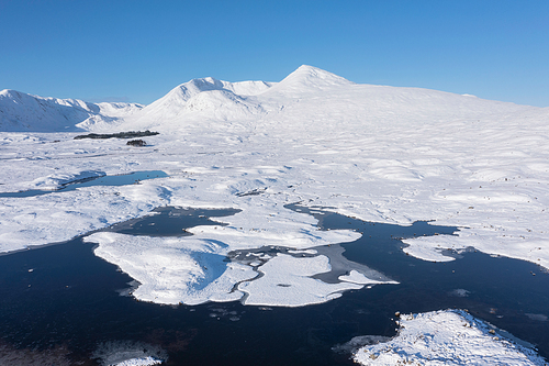 Stunning aerial drone Winter landscape images of Loch Ba and snow covered mountains in background in Scottish Highlands