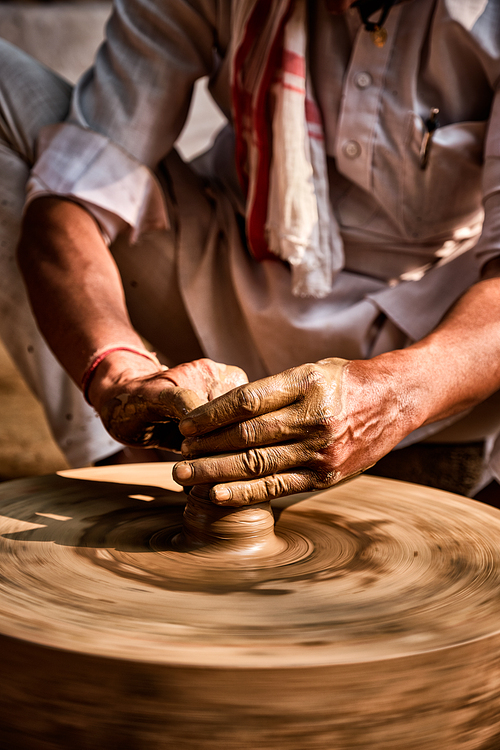 Indian potter at work: throwing the potter's wheel and shaping ceramic vessel and clay ware: pot, jar in pottery workshop. Experienced master. Handwork craft from Shilpagram, Udaipur, Rajasthan, India