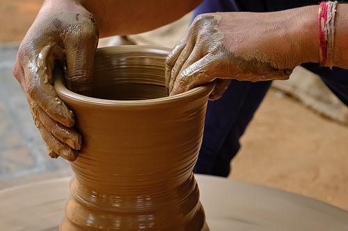 Pottery - skilled wet hands of potter shaping the clay on potter wheel. Pot, vase throwing. Manufacturing traditional handicraft Indian bowl, jar, pot, jug. Shilpagram, Udaipur, Rajasthan, India