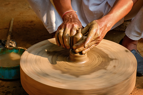 Pottery - skilled hands of potter shaping the clay on potter wheel making small bottle. Pot throwing. Manufacturing traditional handicraft Indian jar, pot, jug. Shilpgram, Udaipur, Rajasthan, India