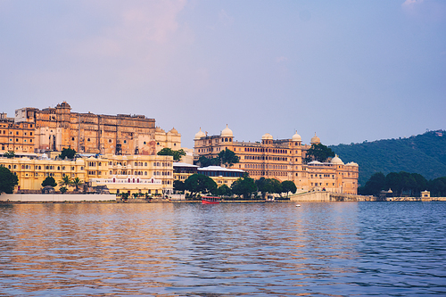 View of famous romantic luxury Rajasthan indian tourist landmark - Udaipur City Palace on sunset with tourist boat. Udaipur, Rajasthan, India