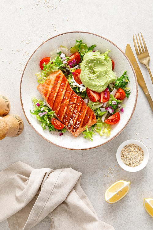 Grilled salmon fish fillet and fresh green lettuce vegetable tomato salad with avocado guacamole. Top view