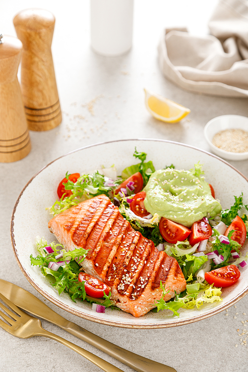 Grilled salmon fish fillet and fresh green lettuce vegetable tomato salad with avocado guacamole
