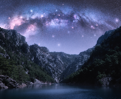 Arched Milky Way and stars over beautiful mountains and sea at night in summer. Colorful landscape with purple starry sky with bright Milky Way arch, constellation, water. Galaxy. Nature and space