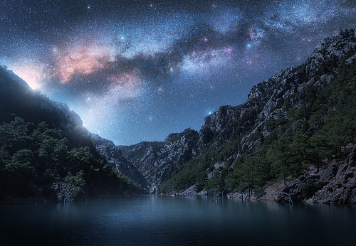 Milky Way and stars over beautiful mountain canyon and blue sea at night in summer. Colorful landscape. Bright starry sky with Milky Way, rocks, trees, fog over the lake. Galaxy. Nature and space