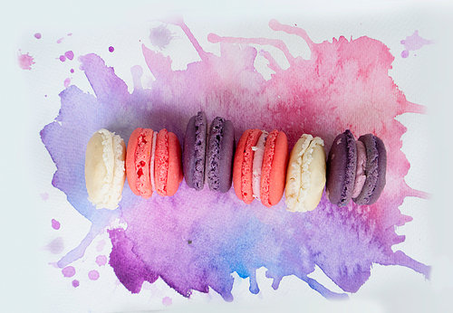 row of french cookies macaroons on watercolor background, top view