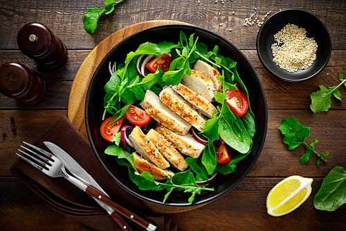 Grilled chicken breast and salad. Fresh vegetable salad with tomato, arugula, spinach and grilled chicken meat in bowl, healthy food, top view.