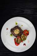 Grilled black angus strip loin steak with vegetables on white plate on black wooden background