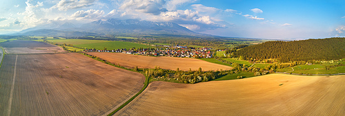 Spring sunny mountain panorama. Village in green forest hills. Agriculture industry. Arable fields. Aerial view of Tatra range. Slovakia farmland valley, Poprad region