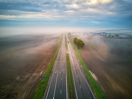 Aerial view of a highway covered by fog. Early misty morning. Road in spring summer fields. Autostrada in rainy weather. Belarus, Minsk region
