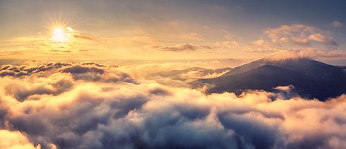 Aerial view of mountains in orange clouds at sunrise in summer. Mountain peak in fog. Beautiful landscape with rocks, hills, sky. Top view from drone. Mountain valley in low clouds. View from above