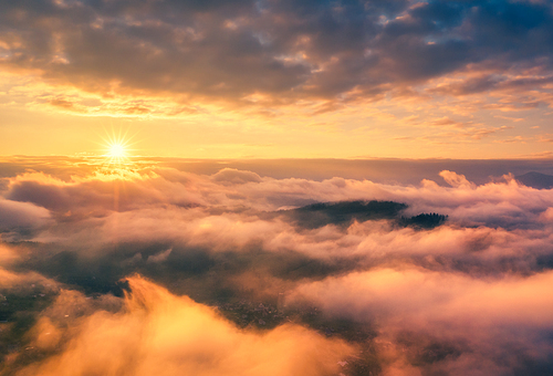 Aerial view of mountains in orange clouds at sunrise in summer. Mountain peak in fog. Beautiful landscape with high rocks, hills, sky. Top view from drone of mountain valley in low clouds. Foggy hills