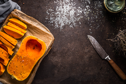 Food background with butternut pumpkin on baking sheet on dark rustic background with knife, top view. Autumn seasonal cooking and eating