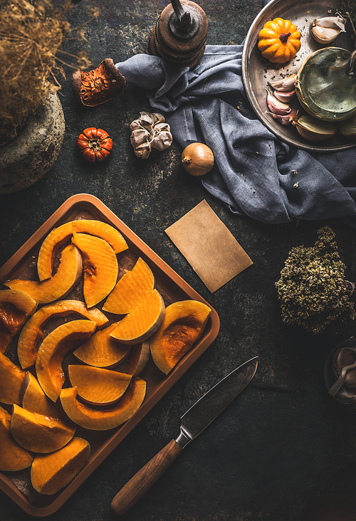 Pumpkin slices on baking sheet on dark rustic kitchen table background with knife and ingredients, top view. Copy space