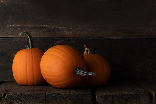 Three whole pumpkins on dark wooden background with copy space for text, halloween or thanksgiving card