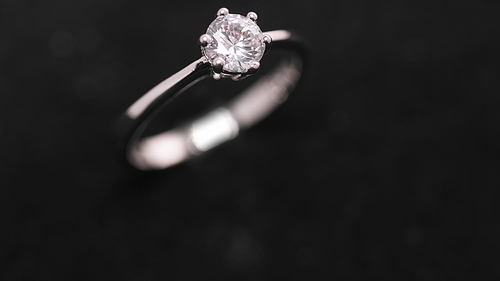 Engagement diamond ring rotating on black background. Traditional piece of jewelry, macro shot. Seamless loop.