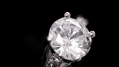 Engagement diamond ring rotating on black background. Traditional piece of jewelry, macro shot.