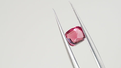 Red spinel gem in tweezers. Jewelry shopping for birthday, Valentine Day, other holiday. Gemologist or jeweller holding burmese spinel, macro shot on gray background