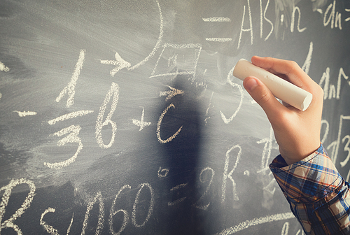 Hand with chalk writting on math formulas black board, retro toned