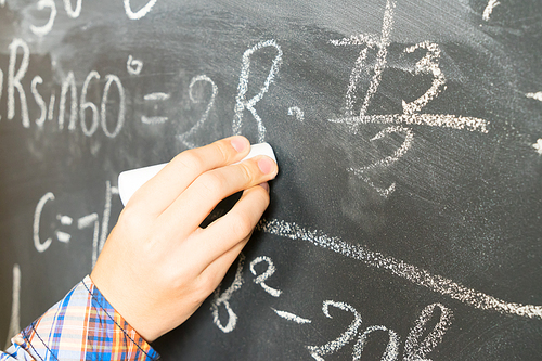 Hand with chalk writting math formulas on black board close up