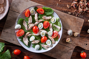 A plate of salad from boiled meat, quail eggs, spinach and tomatoes on a wooden board on the kitchen table. Dietary snack Flat lay