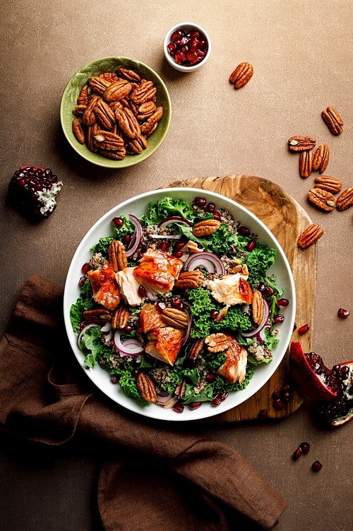 Salmon superfood salad with grilled fish, kale, quinoa, pecan nuts, red onion and pomegranate. Top view