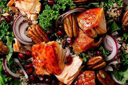 Salmon superfood salad background with grilled fish, kale, quinoa, pecan nuts, red onion and pomegranate. Top view