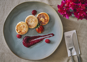 Cottage cheese pancakes or syrniki with raspberry jam on a green plate