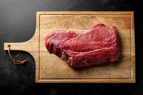 Beef meat entrecote on a cutting board, raw beef meat fillet on black background, top view