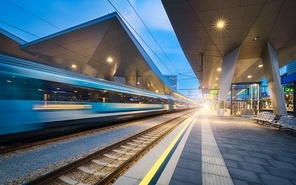 High speed train in motion on the railway station at night. Moving blue modern intercity passenger train, railway platform, architecture, city lights. Modern train station in Vienna, Austria. Railroad