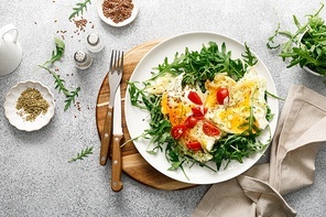 Fried eggs, omelette with onions, tomatoes and fresh arugula salad, top view