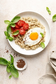 Oatmeal with fried sunny-side-up egg, tomatoes and basil, top view