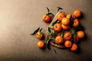 Mandarin oranges, clementines or tangerines with leaves on a dark background, top view