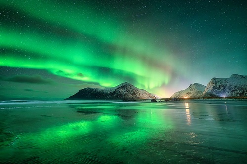 Northern Lights and sandy beach at starry winter night. Lofoten islands, Norway. Beautiful Aurora borealis. Sky with polar lights. Landscape with aurora, sea, sky reflection in water, snowy mountains