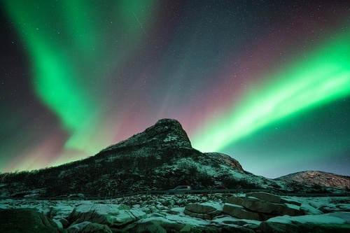 Northern lights and snowy mountains at night in Lofoten, Norway. Aurora borealis above the snow covered rocks. Winter landscape with polar lights, mountain peak. Starry sky with bright aurora