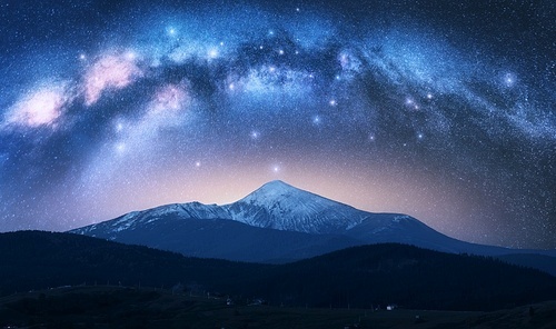 Milky Way over the beautiful Goverla mountain with snow covered peak at night in summer in Ukraine. Colorful landscape with bright starry sky with Milky Way arch, snowy rocks, hills. Space. Nature