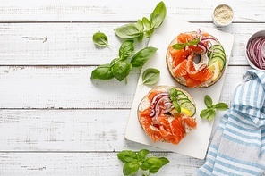 Salmon sandwiches with bagel, salted fish, fresh cucmber, onion and basil on white background, top view. Healthy breakfast with salmon toasts