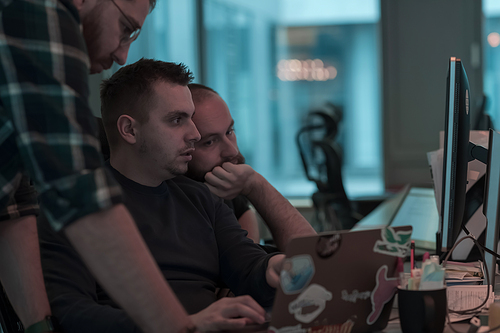 A photo of three men staring intently at a computer while sitting in a modern office. Selective focus. High-quality photo