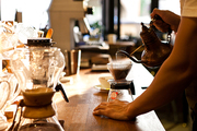 바리스타가 드리퍼에 담긴 커피가루 위로 뜨거운 물을 부어 커피를 추출하는 장면