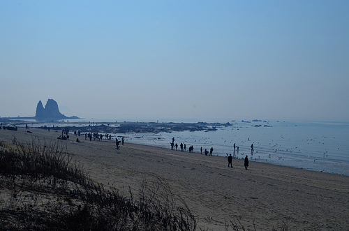제부도 파란 하늘 아래 촛대바위가 보이는 바다 해변가에서 산책하고 있는 사람들
