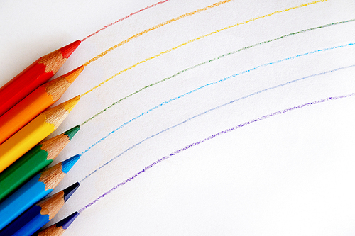 색색깔의 색연필들로 그린 무지개와 그 옆에 놓여있는 색연필들.