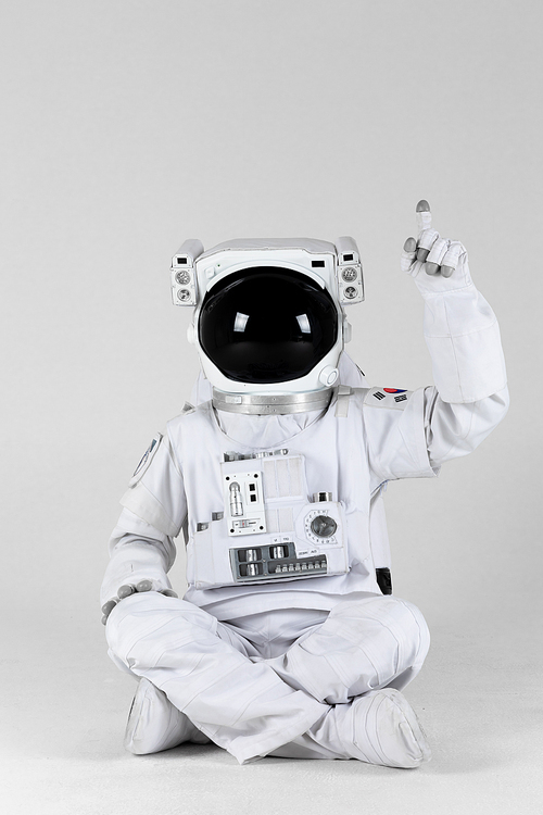 우주 생활 - 바닥에 앉아서 앞 쪽을 손가락으로 가리키고 있는 우주인 앞모습