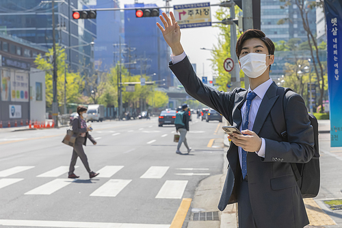 코로나 시대의 신입사원 - 손을 들며 택시를 잡고 있는 마스크 착용한 청년 신입사원