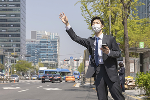 코로나 시대의 신입사원 - 손을 들며 택시를 잡고 있는 마스크 착용한 청년 신입사원