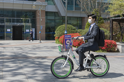 코로나 시대의 신입사원 - 공유 자전거를 타고 출근하는 마스크 착용한 청년 신입사원