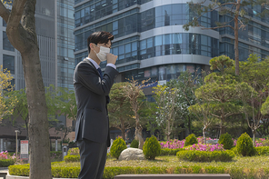 코로나 시대의 신입사원 - 빌딩 앞, 미세먼지로 기침을 하고 있는 마스크 착용한 청년 신입사원