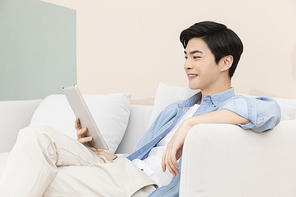 슬기로운 취준생 생활 - 쇼파에 앉아 태블릿 pc를 하며 웃는 청년