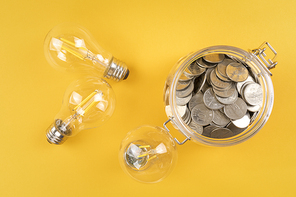 생활 속 에너지 - 노란색 배경지 위에 놓여진 투명한 전구들과 유리병에 담겨진 동전들