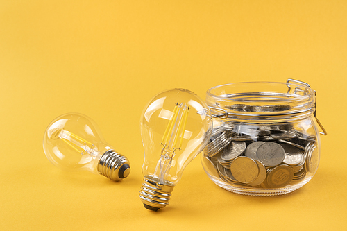 생활 속 에너지 - 노란색 배경지 위에 놓여진 투명한 전구들과 유리병에 담겨진 동전들
